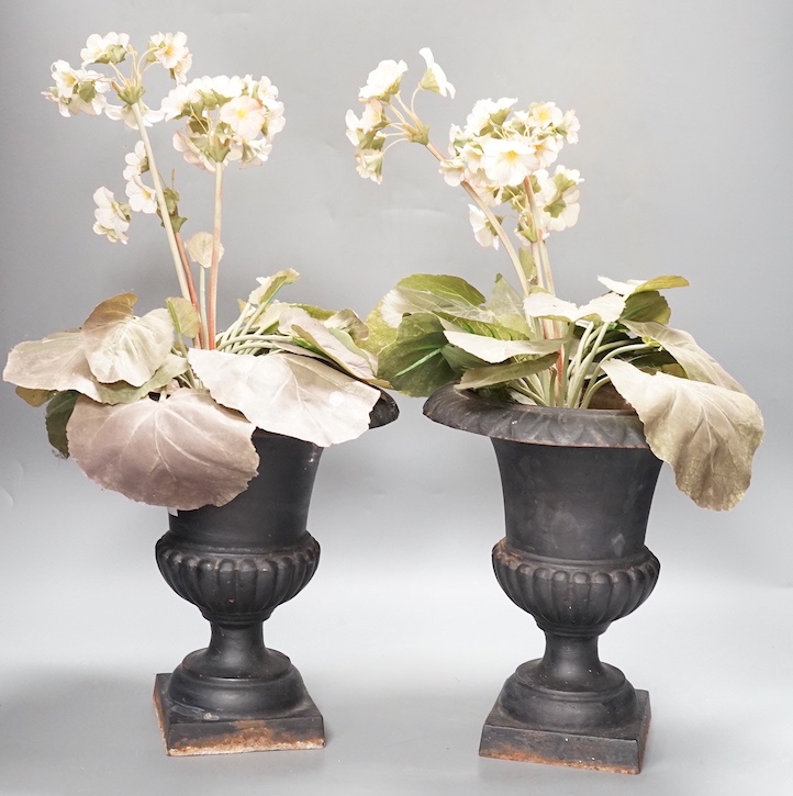 A pair of cast iron urns 25cm, containing faux plants